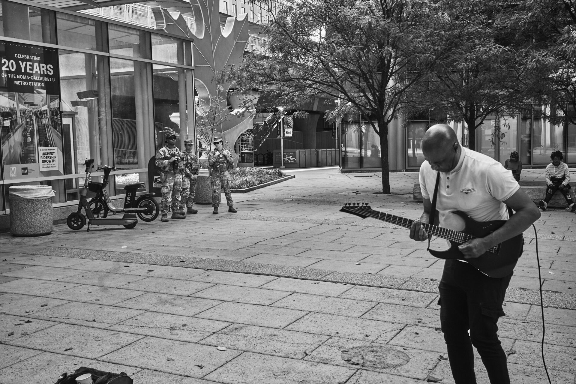 National Guard watch a busker play guitar