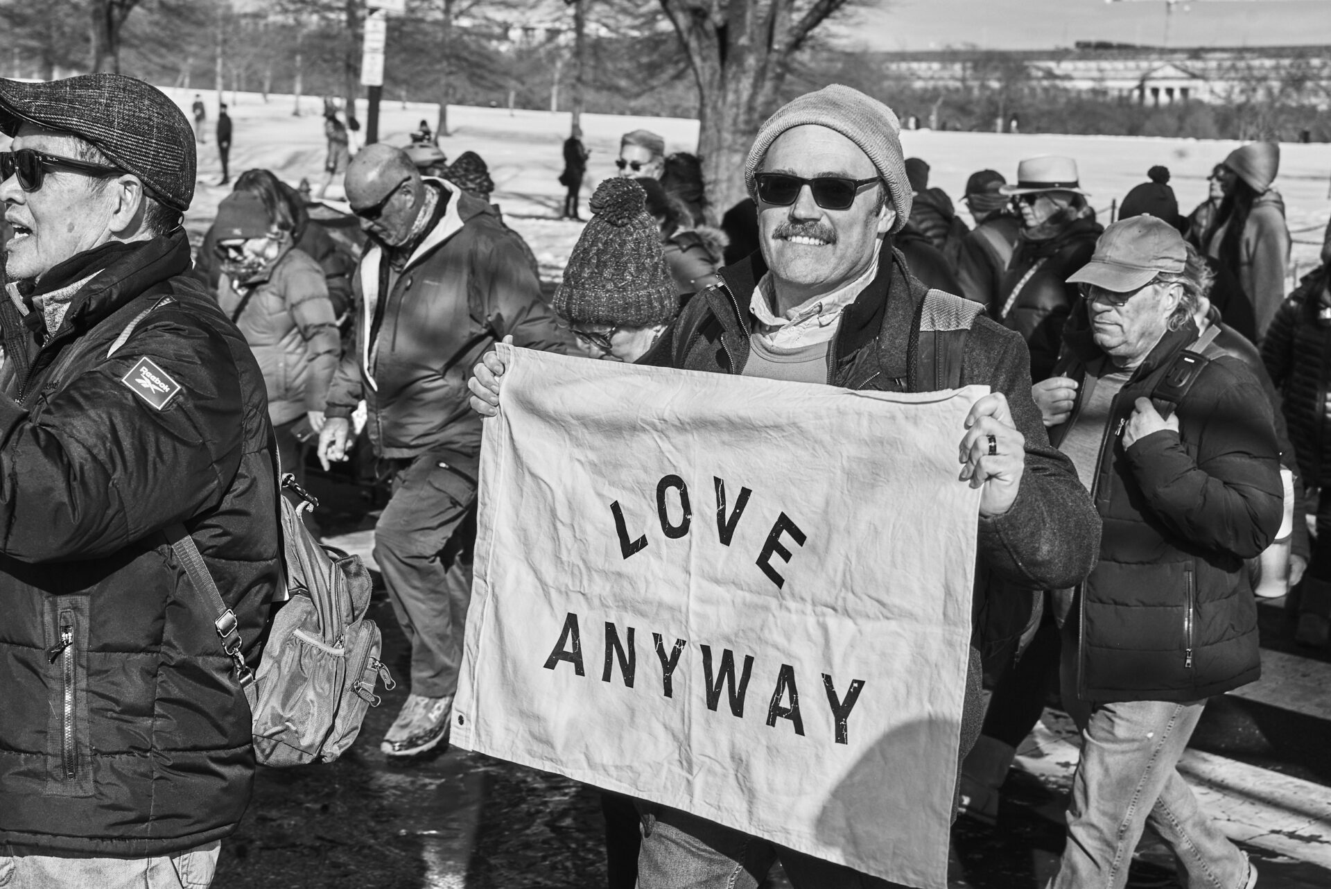 A man holds up a flag reading "Love Anyway"