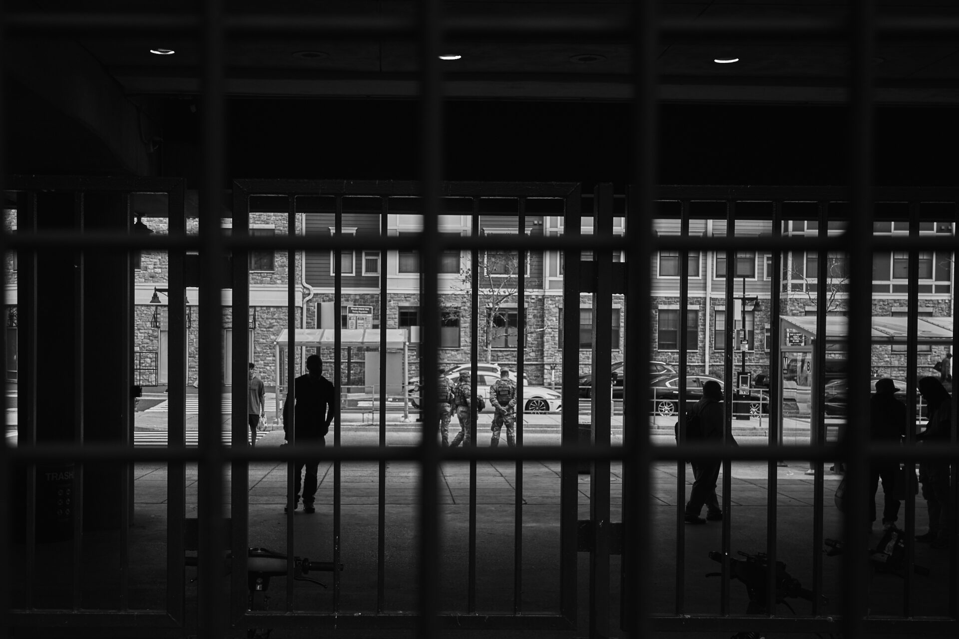 Silhouettes of people lurk in the back of bars at a metro station. National Guard can be seen in the distance