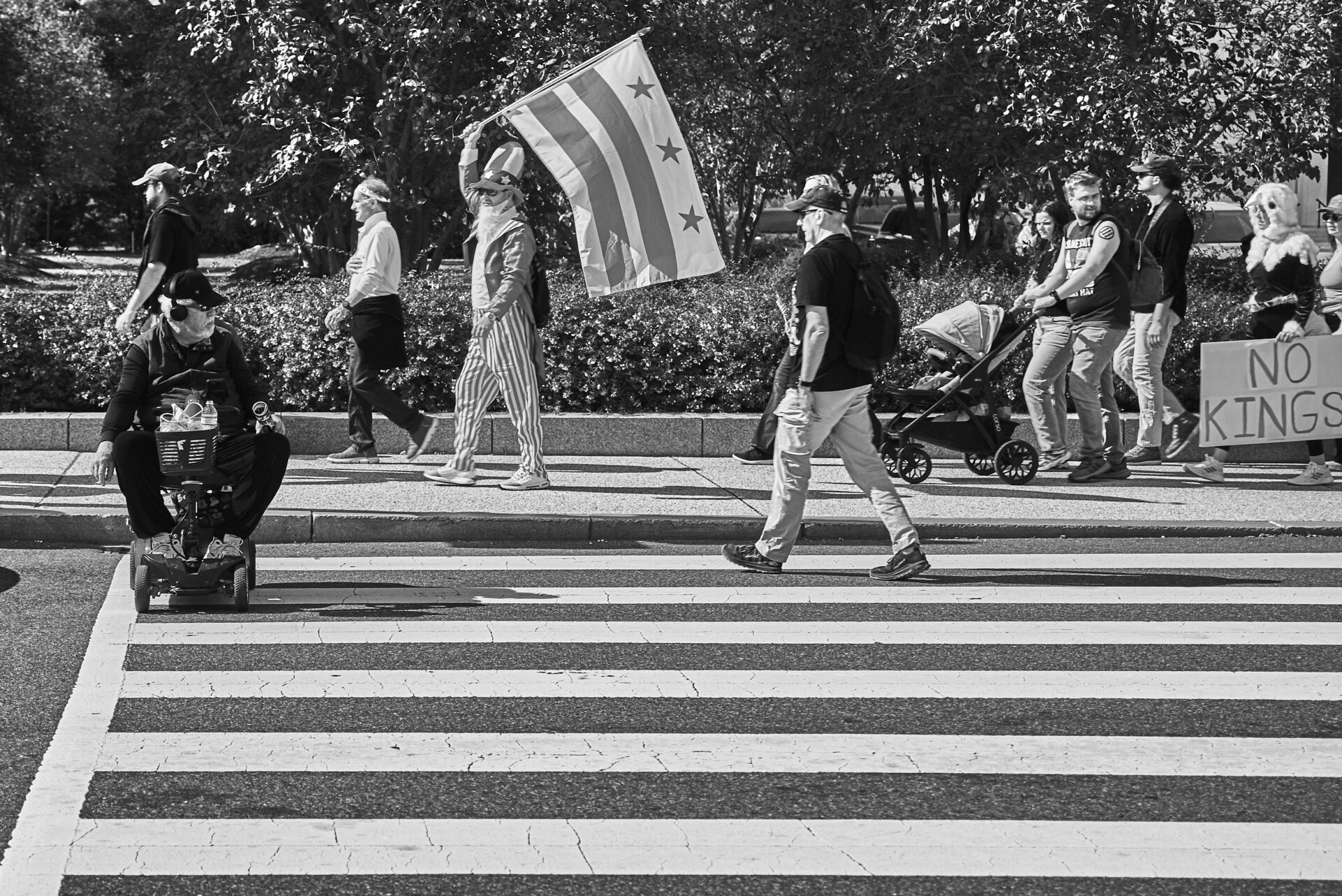 A man in a wheelchair looks on as protestors walk by carrying the DC flag