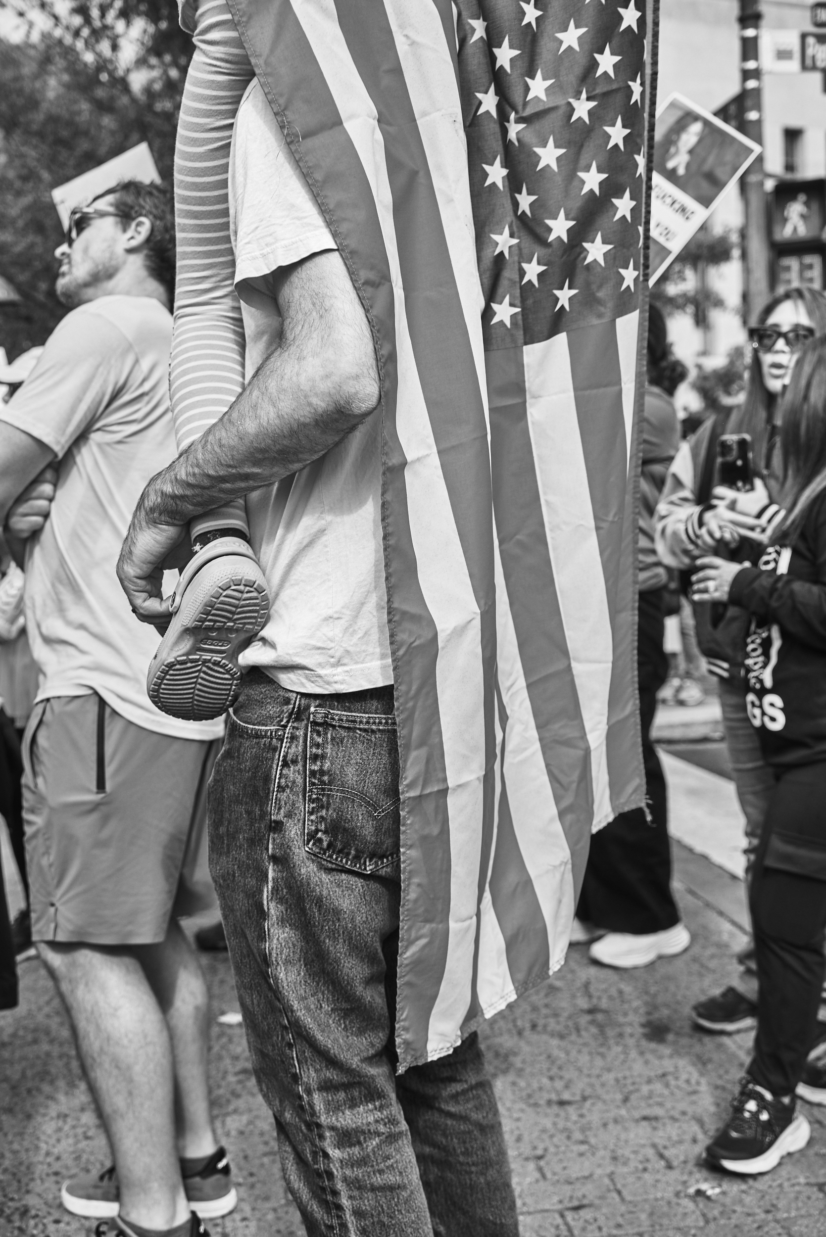 An american flag is draped around the neck of someone carrying a child on their back