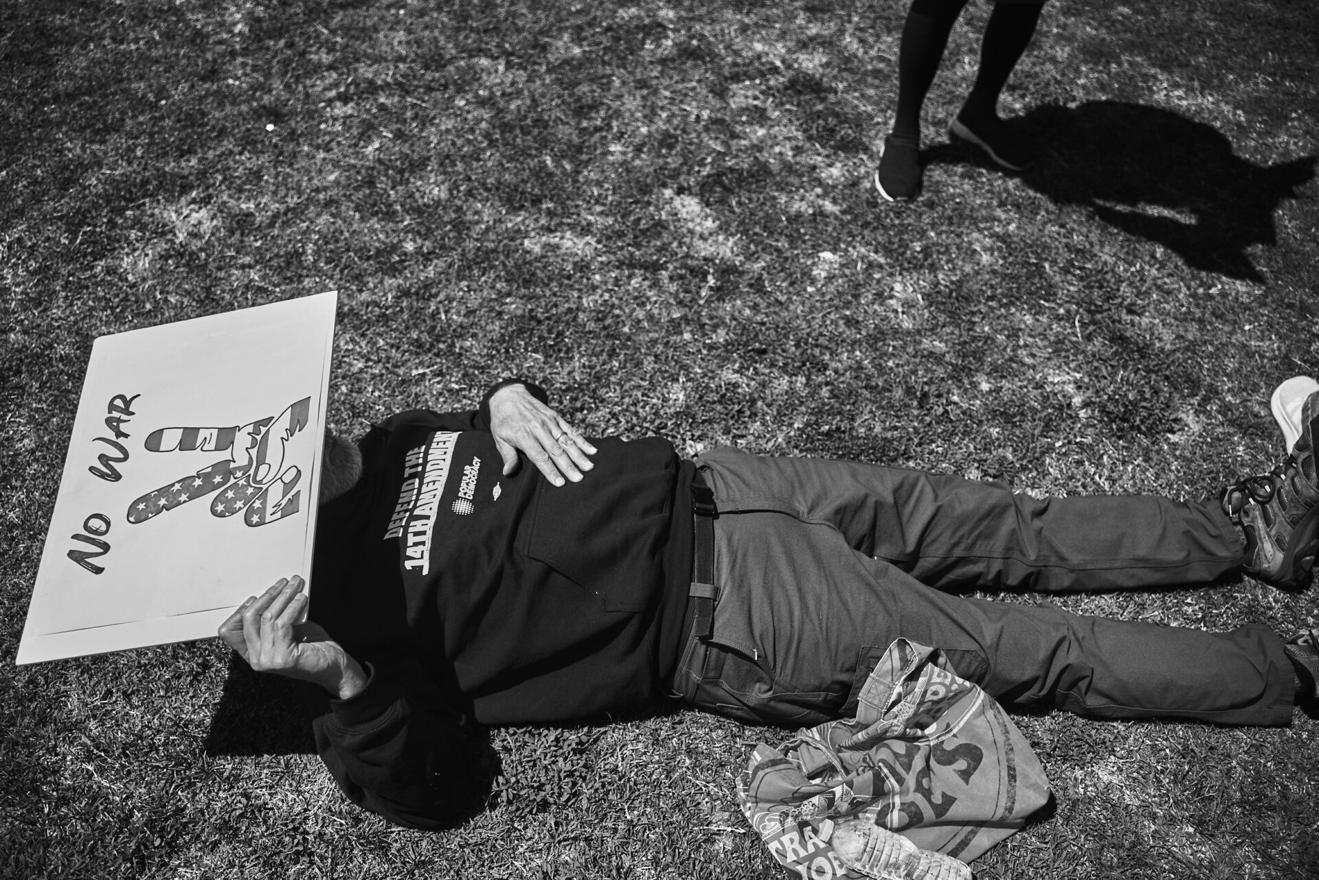 A man lies on teh ground shielding his face from the sun with a protest sign