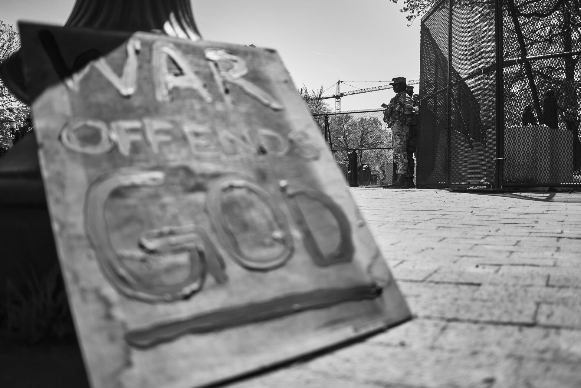 In the foreground, a sign that reads "War offends god" is propped against a pole. In the background, a national guardsman stands on watch.